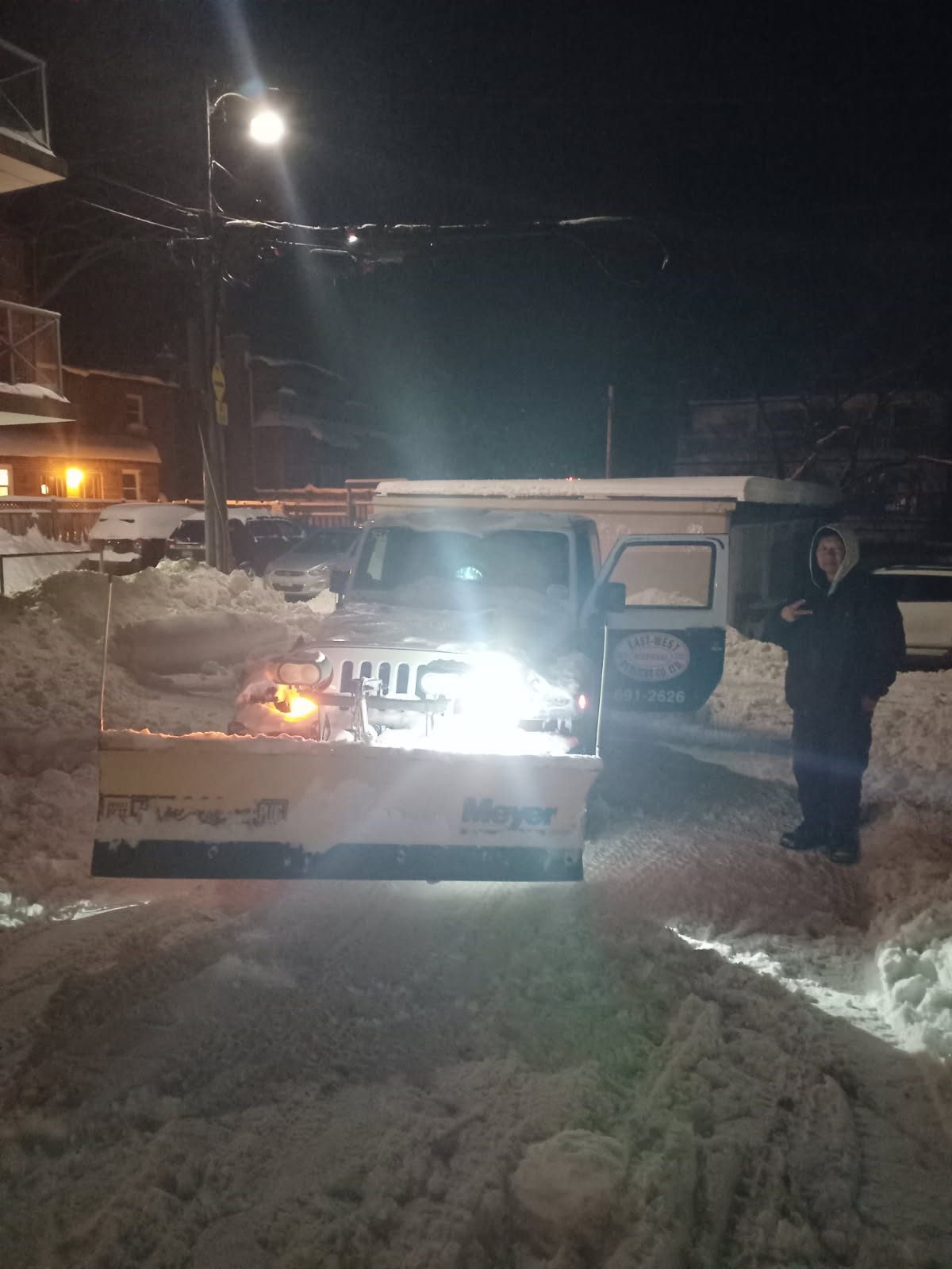 East-West plow truck working overnight under headlights clearing snow at a Toronto commercial property