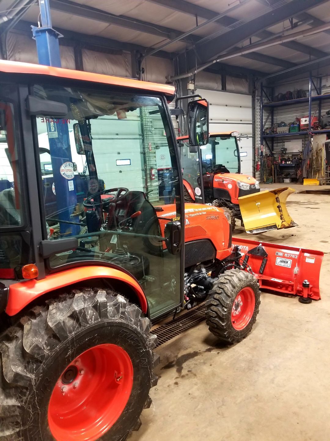 Kubota sidewalk snow machine with plow blade being serviced inside the East-West maintenance shop